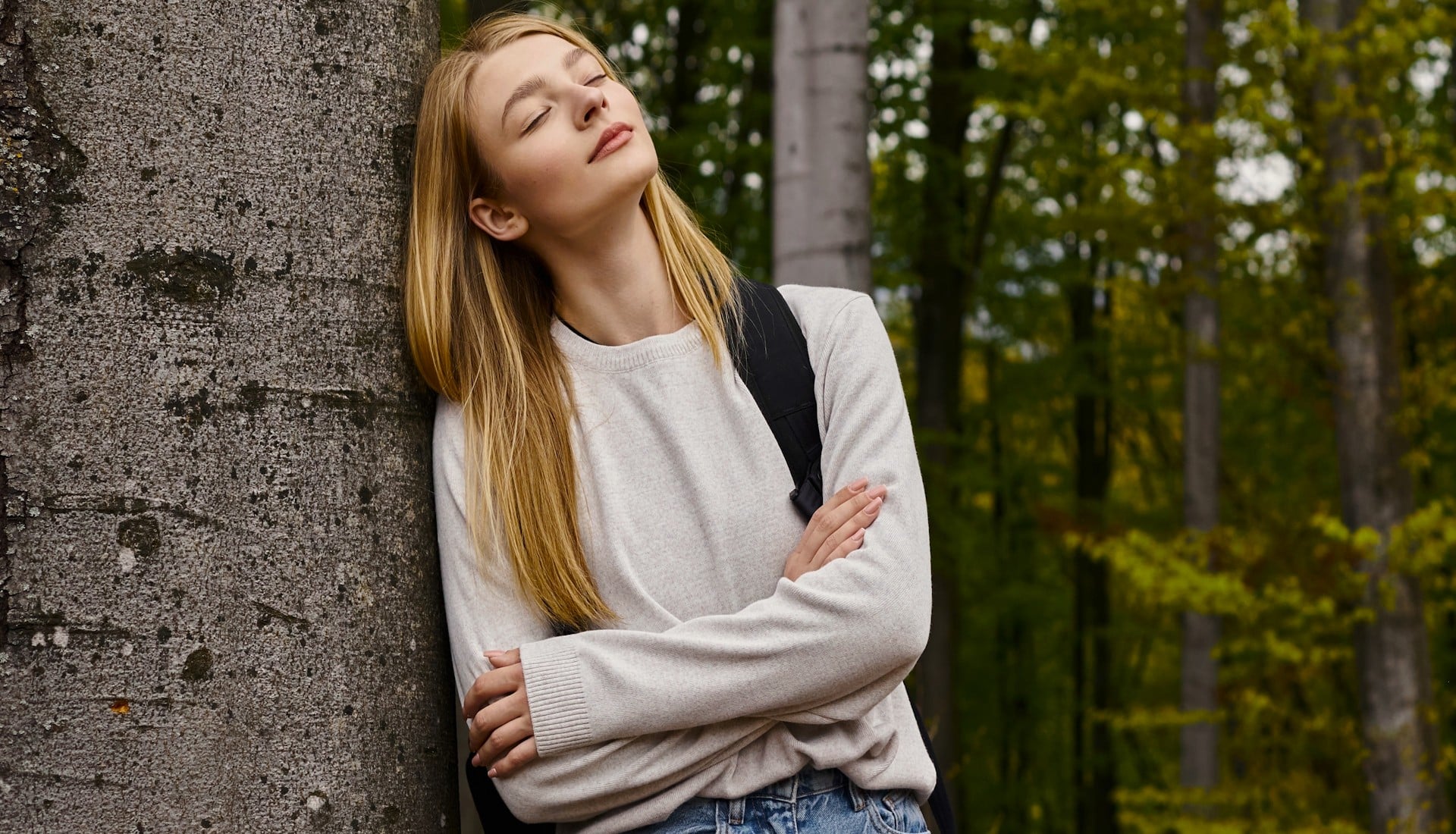 Junge Dame lehnt am Baum im Wald und träumt